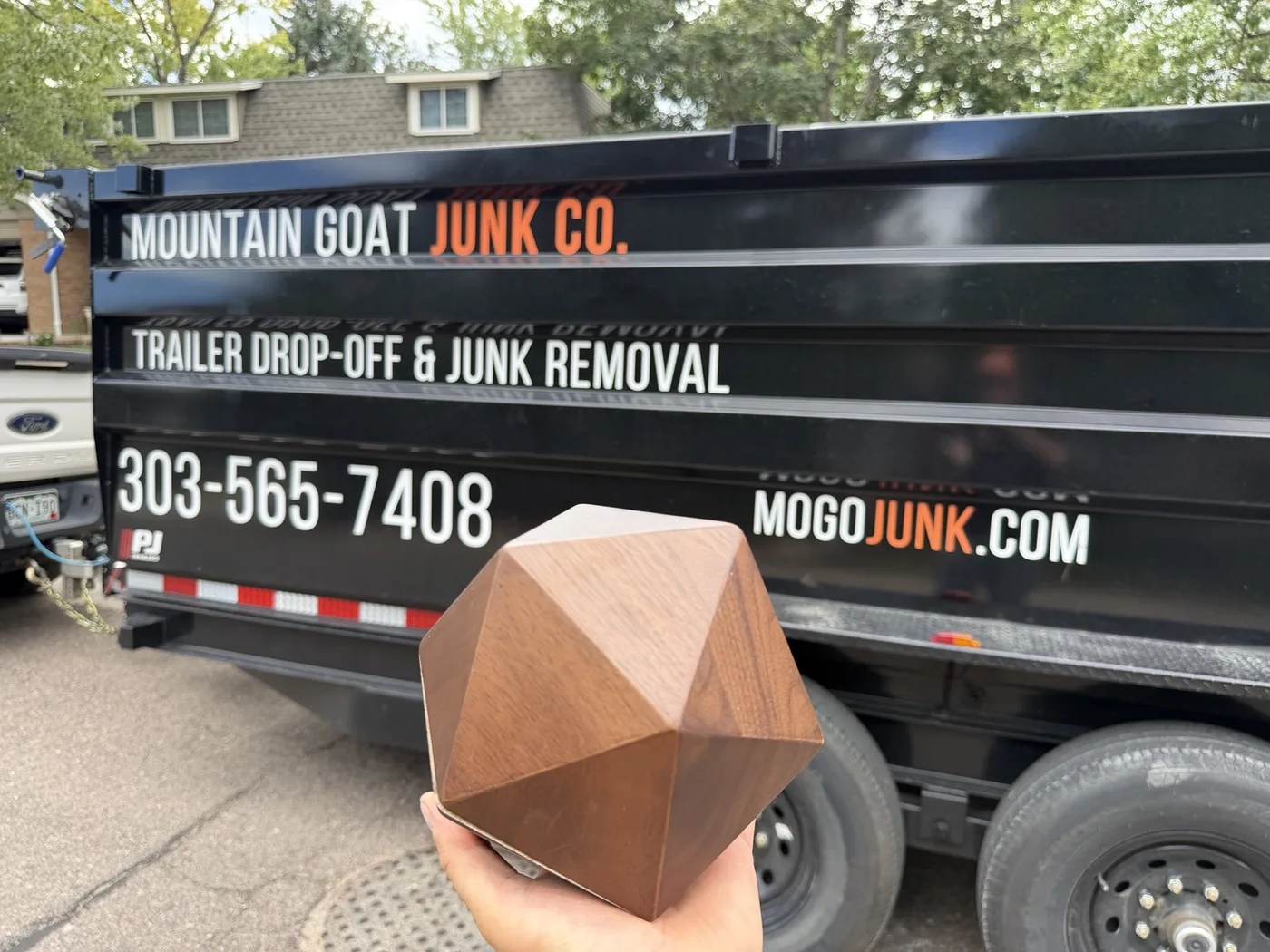Decorative urn from an Englewood warehouse cleanout held in front of a Mountain Goat Junk Co. dump trailer
